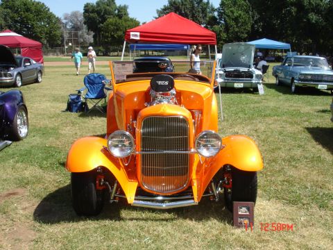 1978 Ford Mustang II - Outdoor car show features a bright orange custom hot rod with a prominent engine and chrome details.