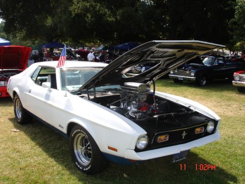 1978 Ford Mustang II - A white classic car with its hood up at an outdoor event, displaying its engine and an American flag.