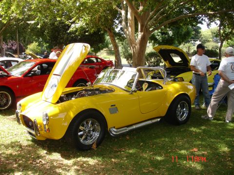 1978 Ford Mustang II - A yellow convertible sports car is displayed outdoors with its hood open, alongside other vehicles.