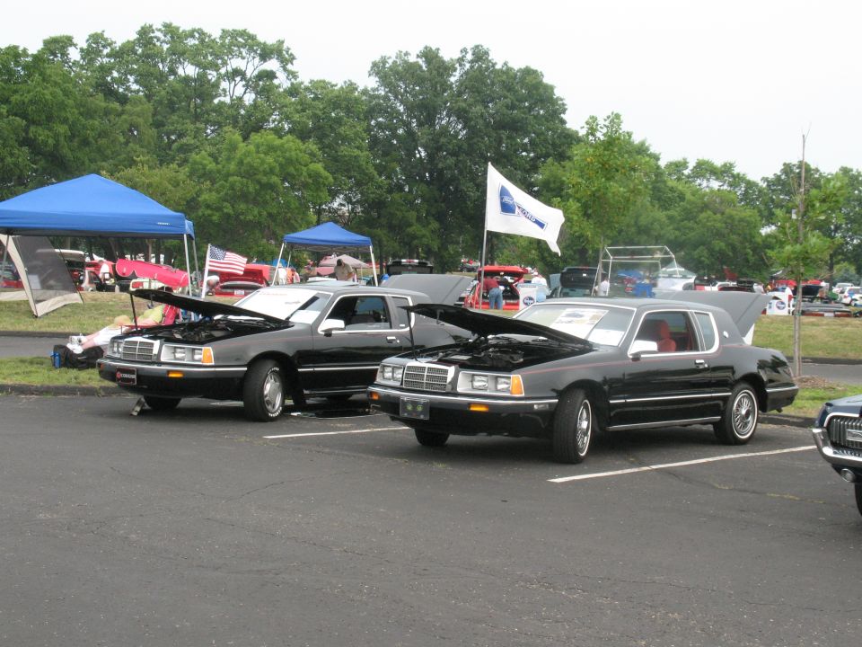 Two black 1985 Mercury Cougars parked side-by-side with hoods open at a car show