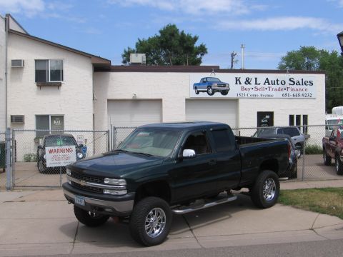 2001 Chevrolet Silverado 1500 - A dark green 2001 Chevrolet Silverado 1500 pickup truck is parked in front of K & L Auto Sales, which displays its address and phone number.