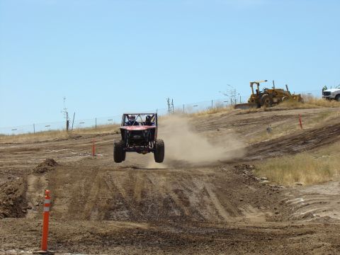 1989 Ford Bronco - Off-road buggy airborne over a dirt track during an event.