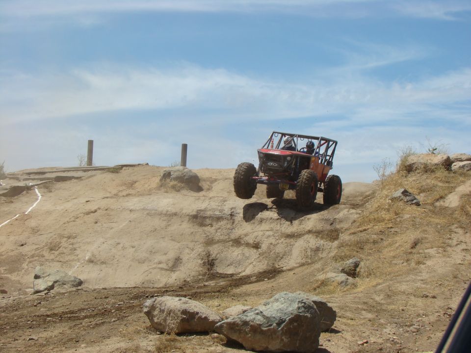 Red off-road buggy with a roll cage jumping over a dirt mound