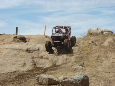 1989 Ford Bronco - An off-road buggy navigates a challenging dirt and rock obstacle course under a partly cloudy sky.