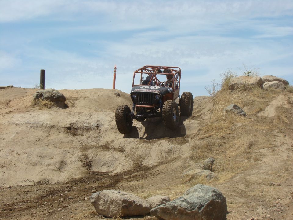 Orange off-road buggy with roll cage climbing a rocky dirt hill