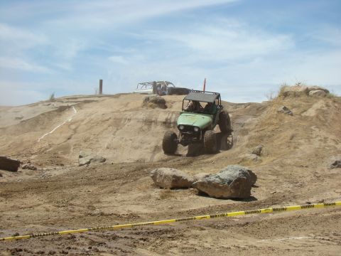 1989 Ford Bronco - An off-road race is underway with vehicles navigating a challenging dirt terrain under a partly cloudy sky.