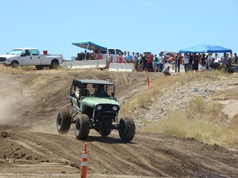 1989 Ford Bronco - A custom off-road buggy navigates a dusty track during a race event, with a crowd watching from the sidelines.