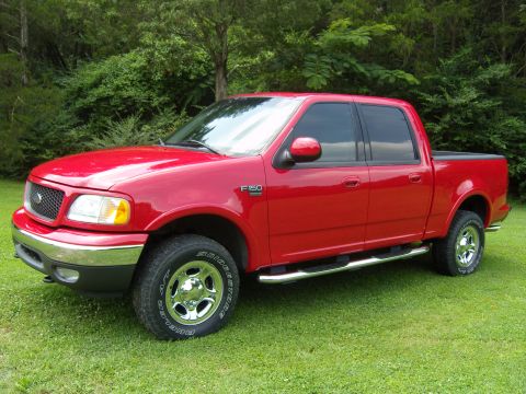 2007 Ford Mustang - Red four-door pickup truck parked on a grassy lawn with trees in the background. The F-150 badge is visible on the fender.