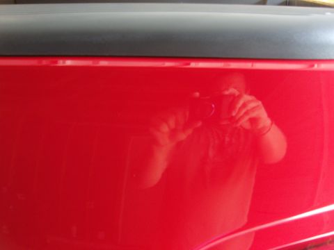 2007 Ford Mustang - A person's reflection is visible in the glossy red paint of a vehicle panel.