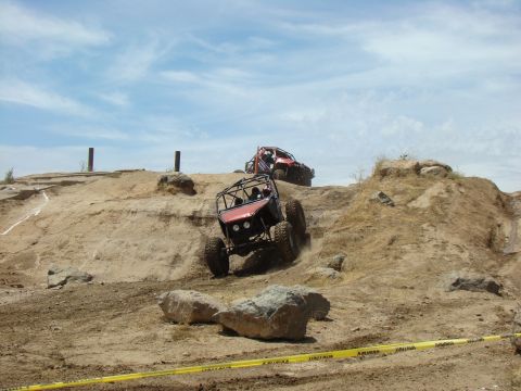 1989 Ford Bronco - Off-road vehicles tackle a challenging dirt incline under a partly cloudy sky.