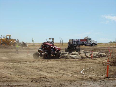 1989 Ford Bronco - Custom off-road vehicles tackle a challenging course with construction equipment and a large truck nearby.