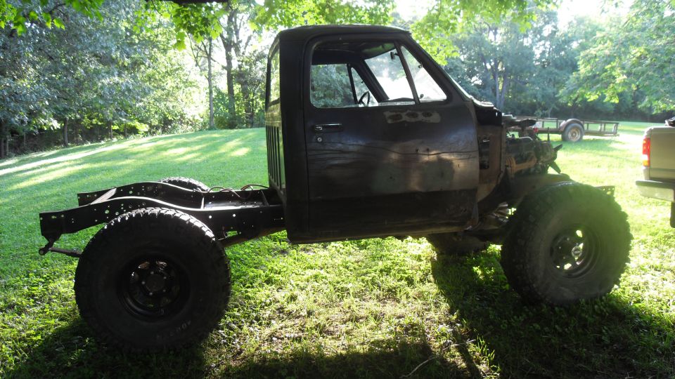 Side view of a black 1980s Dodge pickup truck chassis with cab, missing body panels