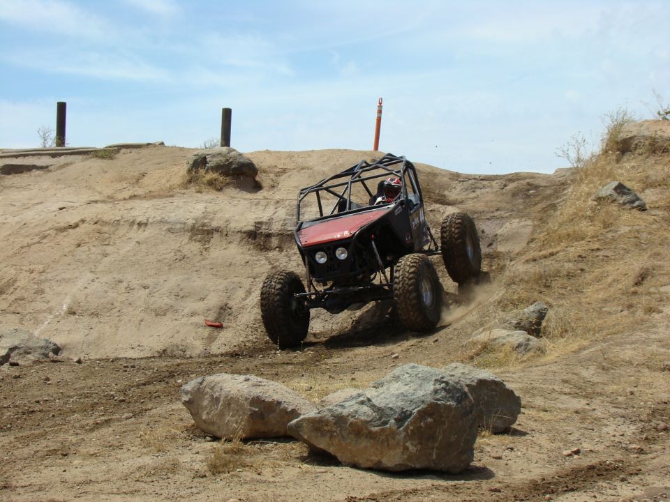 Custom off-road buggy with roll cage climbing a steep dirt hill with large tires