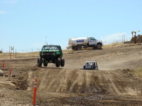 1989 Ford Bronco - Off-road vehicles compete on a dirt track under a clear blue sky.