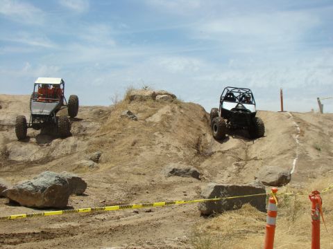 1989 Ford Bronco - Two custom off-road vehicles navigate a challenging rocky terrain on a sunny day.