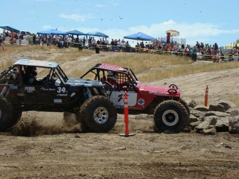 1989 Ford Bronco - Two custom off-road vehicles compete on a rocky, dusty course under a bright, sunny sky.