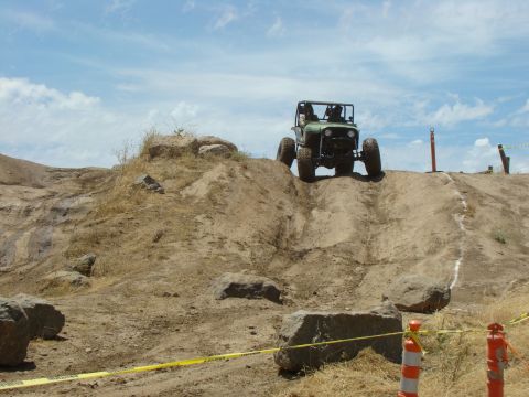 1989 Ford Bronco - A modified off-road vehicle navigates a challenging dirt course under a partly cloudy sky.