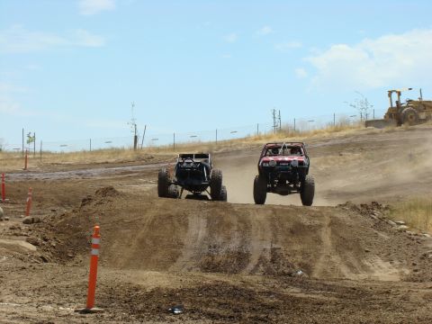 1989 Ford Bronco - Two custom off-road vehicles compete on a dusty track, kicking up dirt as they navigate the terrain.