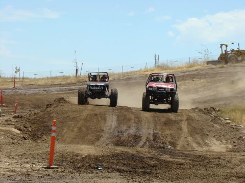 1989 Ford Bronco - Custom off-road vehicles compete on a dusty track under a clear sky.