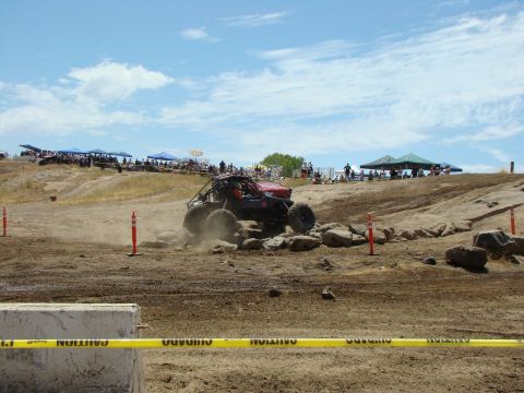1989 Ford Bronco - An off-road buggy tackles a challenging rock course with spectators watching from the hillside.