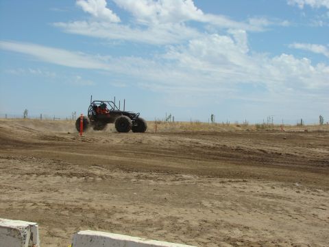 1989 Ford Bronco - A custom off-road buggy navigates a dusty track under a partly cloudy sky.