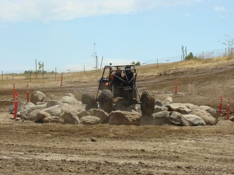 1989 Ford Bronco - A custom off-road buggy navigates a challenging rock obstacle on a dusty track under a clear sky.