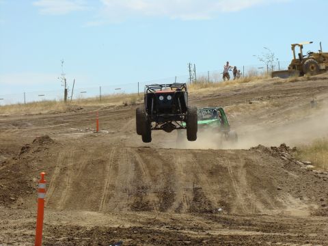 1989 Ford Bronco - Two off-road buggies compete in a race, with one vehicle airborne over a dirt jump.
