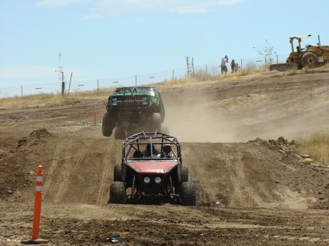 1989 Ford Bronco - Off-road vehicles compete on a dusty track with spectators and construction equipment nearby.
