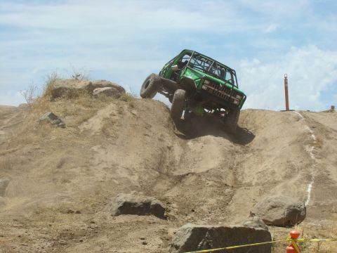 1989 Ford Bronco - A modified green off-road vehicle navigates a steep dirt incline during a race.