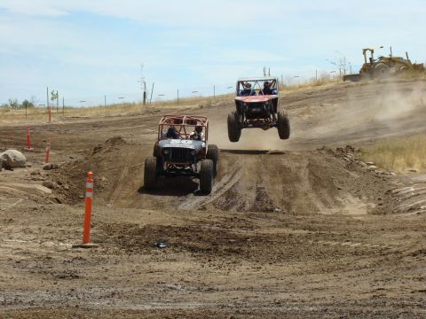 1989 Ford Bronco - Off-road buggies compete on a dirt track, with one vehicle airborne over a jump.