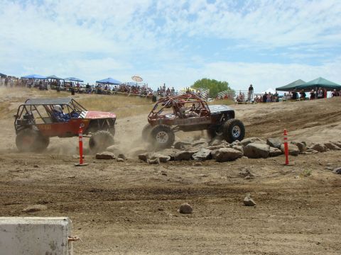 1989 Ford Bronco - These custom off-road vehicles are competing on a challenging, rocky terrain with a crowd watching.