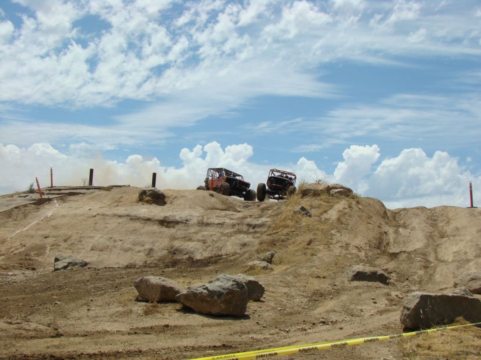 Two off-road vehicles climb a rocky hill under a cloudy sky
