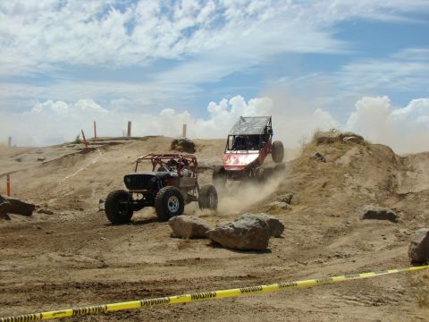 1989 Ford Bronco - Two custom-built off-road vehicles compete on a challenging dirt course, kicking up dust as they navigate the rocky landscape.