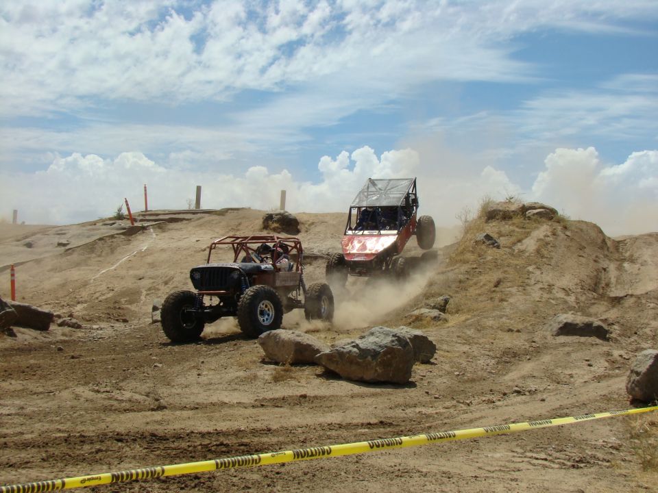 Two off-road buggies race on a dusty, rocky terrain under a cloudy sky