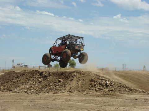 1989 Ford Bronco - A custom off-road buggy soars through the air during a race, with a white pickup truck visible in the distance.
