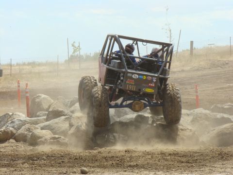 1989 Ford Bronco - Custom off-road buggy tackles a rocky obstacle course, sending dust flying.