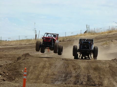 1989 Ford Bronco - Two custom off-road vehicles compete on a dusty track, with one vehicle mid-air.
