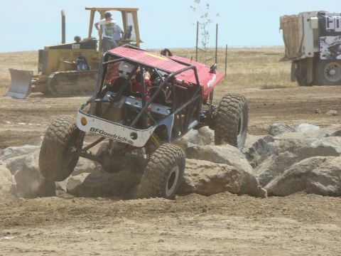 1989 Ford Bronco - A custom off-road buggy tackles a rocky obstacle course, with a bulldozer and dump truck in the background.