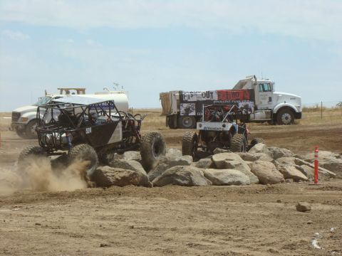 1989 Ford Bronco - Custom off-road vehicles tackle a challenging rock obstacle course under a bright sky.