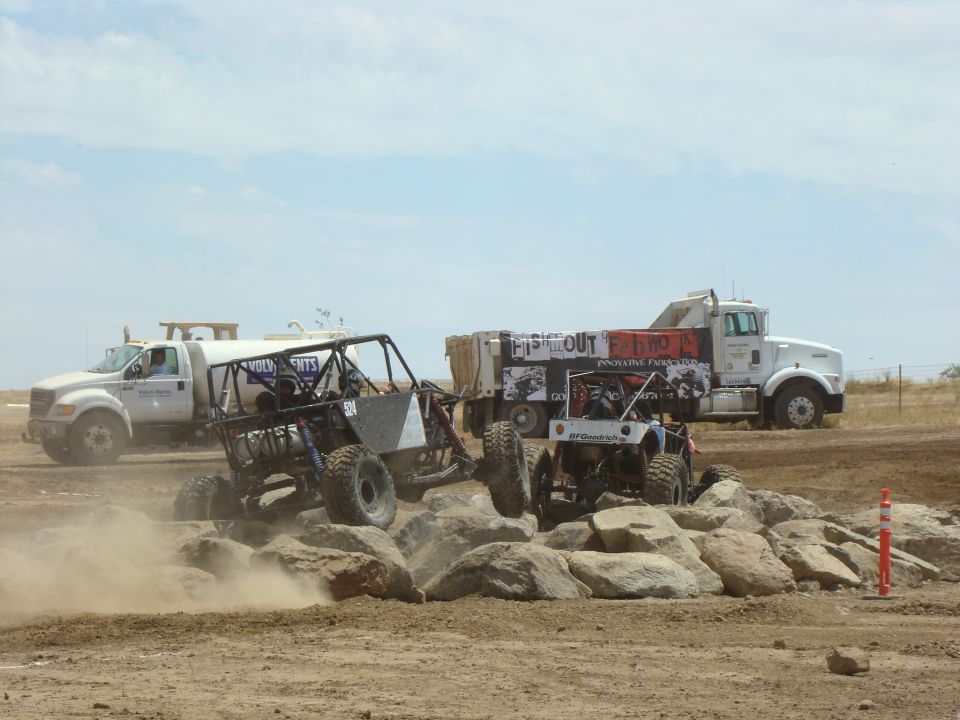 Off-road buggies navigate a rocky obstacle course with a large dump truck in the background