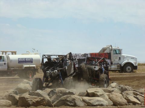 1989 Ford Bronco - Off-road buggies navigate a rocky course during a race, with support vehicles visible in the background.