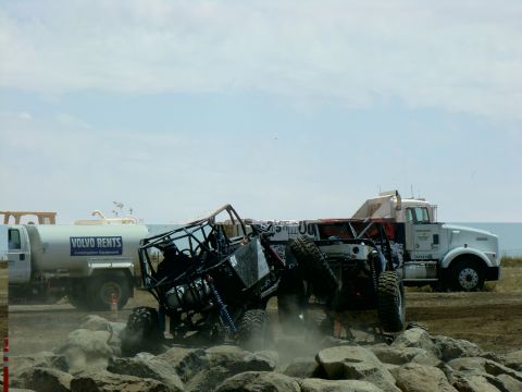 1989 Ford Bronco - An off-road buggy attempts to traverse a rocky terrain, with support vehicles nearby.