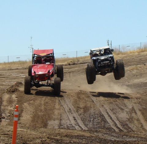 1989 Ford Bronco - Off-road buggies compete in a race, with one vehicle mid-air over a dirt jump.