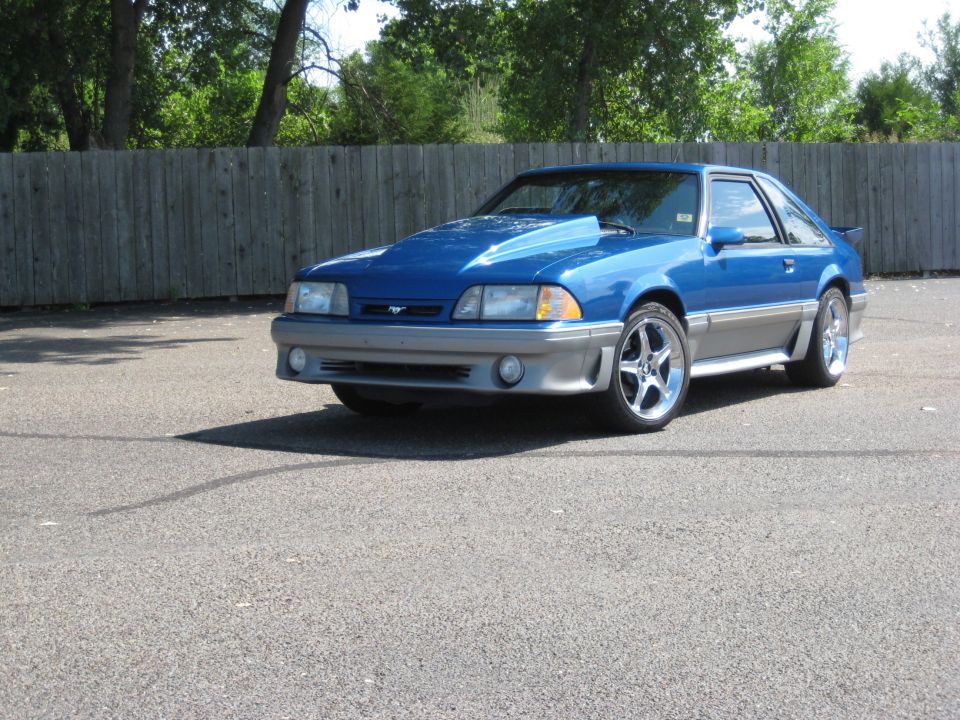 Blue 1990 Ford Mustang parked outside with a wooden fence behind it