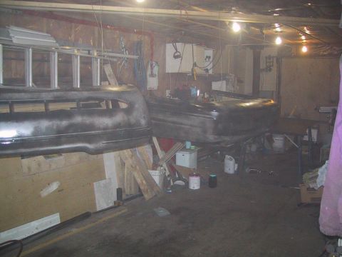 2003 Ford Crown Victoria - Two car body parts, a bumper and a hood, are visible in a cluttered garage setting, suggesting they are undergoing preparation for a paint…