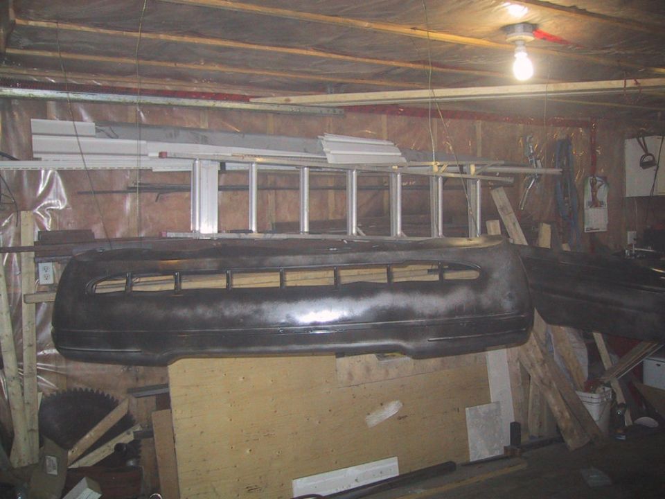 Ford Crown Victoria front bumper hanging in garage, with ladder and tools in background