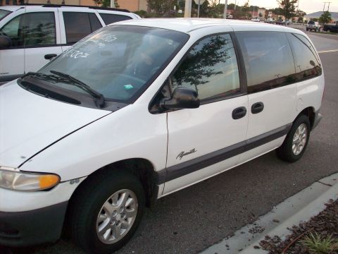 1985 Ford Bronco - A white minivan is parked next to a white SUV on a paved surface.