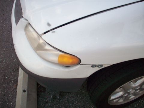 1985 Ford Bronco - The front corner of a white vehicle is visible, with a clear turn signal and some scuff marks on the paint.