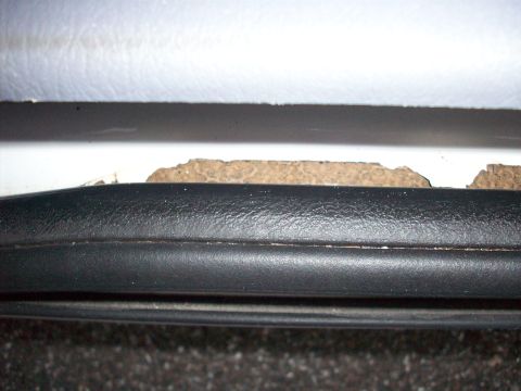 1985 Ford Bronco - The lower door sill of a vehicle shows damage with exposed insulation material beneath the trim.