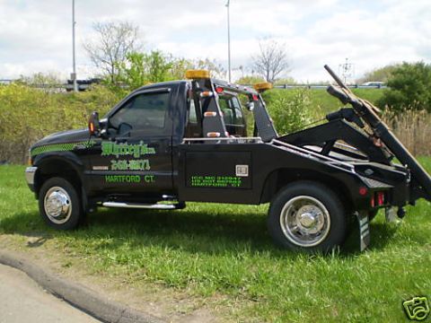 1990 Ford Bronco - Tow truck parked on grassy shoulder near a highway.